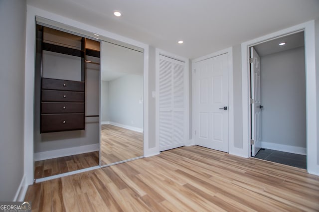 unfurnished bedroom with recessed lighting, two closets, wood finished floors, and baseboards