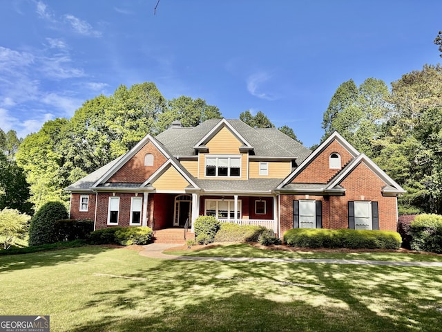 craftsman-style house with a front yard, a chimney, a porch, and brick siding