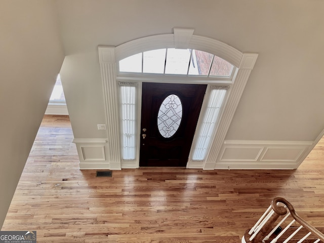 entryway with a decorative wall, visible vents, wainscoting, and wood finished floors