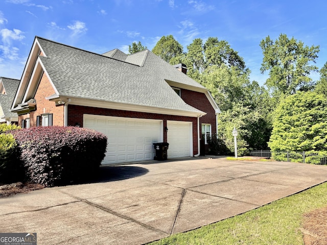 view of property exterior featuring driveway, roof with shingles, fence, brick siding, and a garage