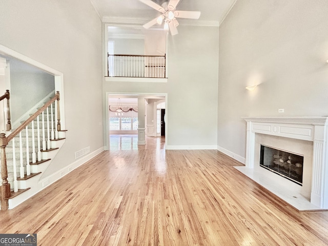 unfurnished living room with stairway, ornamental molding, light wood-type flooring, visible vents, and a fireplace with flush hearth