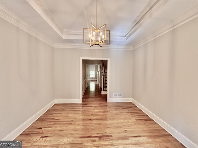 unfurnished dining area with a chandelier, light wood-style floors, ornamental molding, visible vents, and a tray ceiling