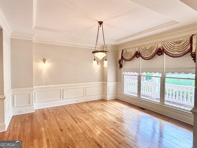 unfurnished dining area with visible vents, light wood-style floors, crown molding, and a tray ceiling
