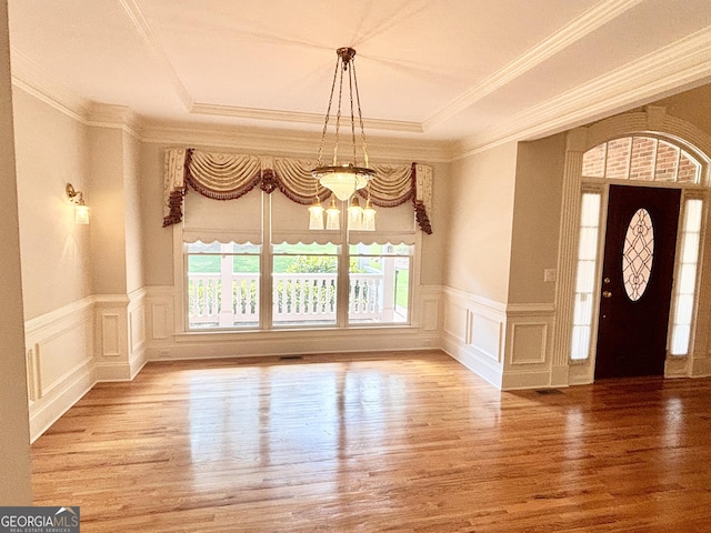 foyer featuring wood finished floors, a decorative wall, a chandelier, wainscoting, and ornamental molding