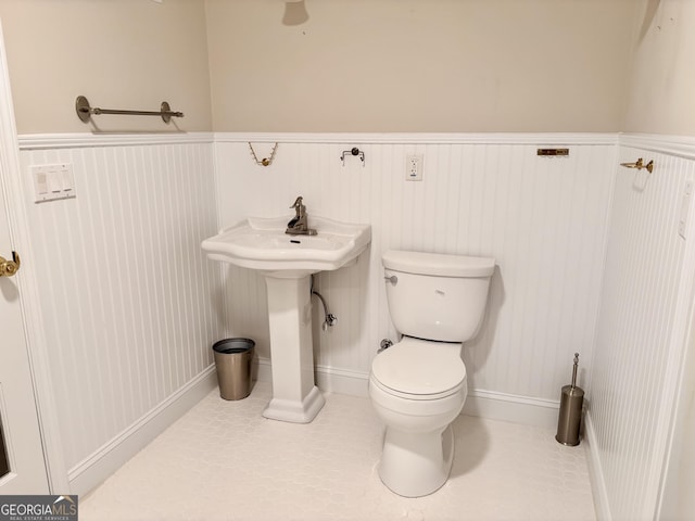 bathroom featuring toilet, a wainscoted wall, a sink, and tile patterned floors
