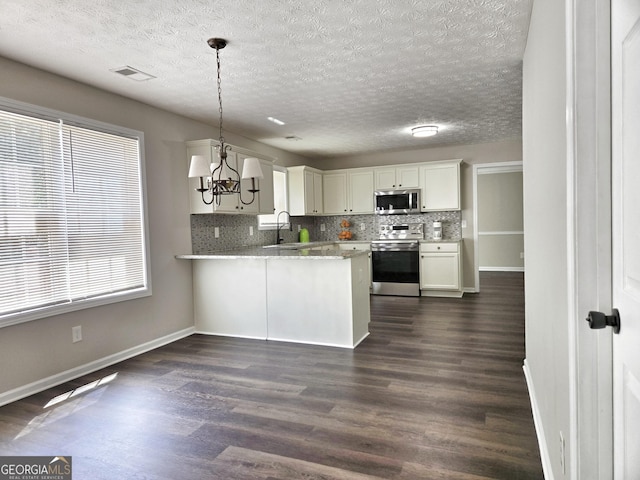 kitchen featuring tasteful backsplash, appliances with stainless steel finishes, an inviting chandelier, dark wood-type flooring, and a peninsula