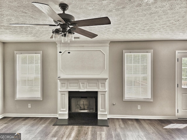 unfurnished living room featuring a fireplace with raised hearth, a ceiling fan, baseboards, a textured ceiling, and wood finished floors