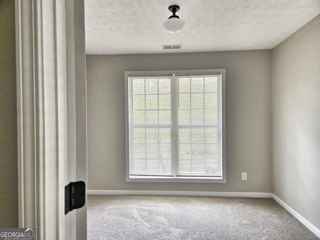 carpeted empty room featuring baseboards, visible vents, a wealth of natural light, and a textured ceiling