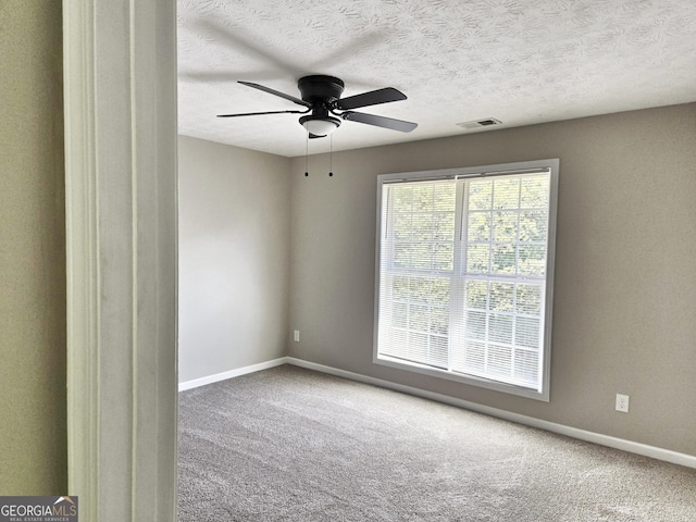 empty room featuring carpet flooring, ceiling fan, visible vents, baseboards, and a textured ceiling