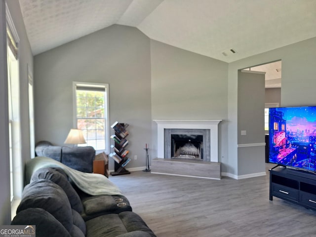 living room featuring a fireplace, visible vents, vaulted ceiling, baseboards, and wood finished floors