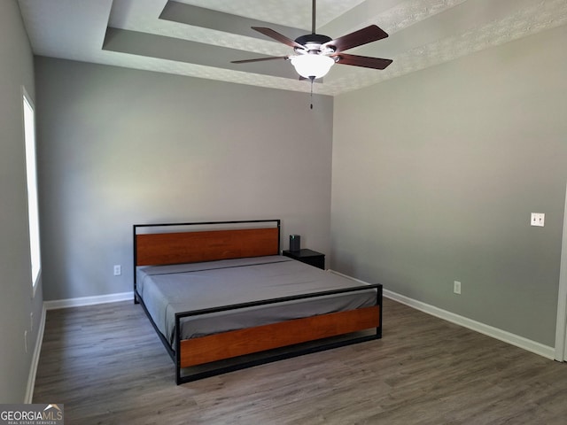 bedroom featuring a raised ceiling, wood finished floors, ceiling fan, and baseboards