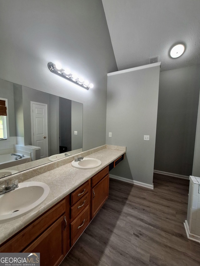 bathroom with double vanity, wood finished floors, a garden tub, and a sink