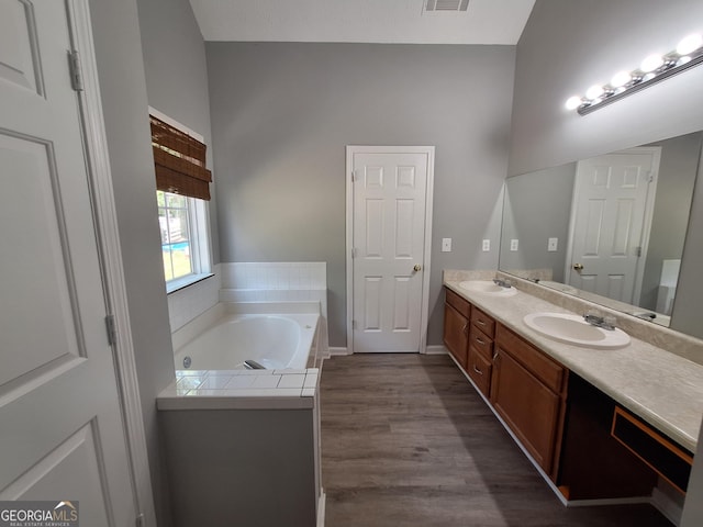 full bath with double vanity, wood finished floors, a garden tub, and a sink