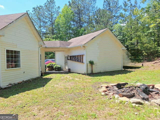 view of side of home with a yard, a shingled roof, and an outdoor fire pit