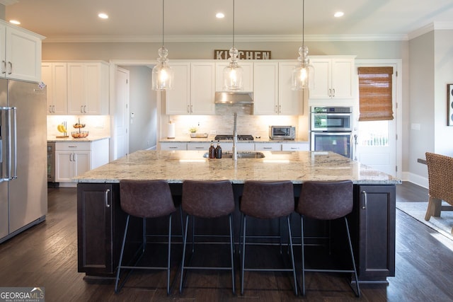 kitchen with a kitchen island with sink, white cabinetry, appliances with stainless steel finishes, and under cabinet range hood