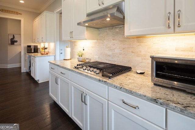 kitchen with light stone countertops, white cabinets, stainless steel gas stovetop, ornamental molding, and under cabinet range hood
