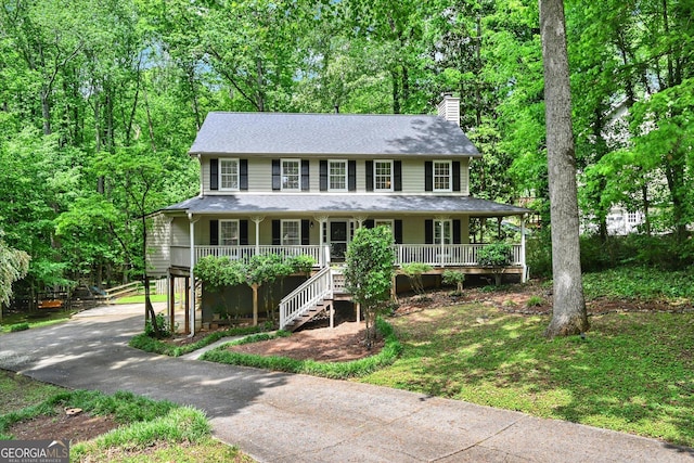 colonial-style house with covered porch, stairs, a chimney, and driveway