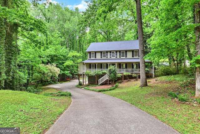 view of front of house with covered porch, asphalt driveway, stairway, roof with shingles, and a forest view