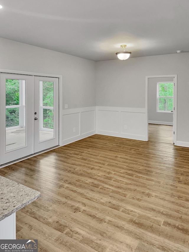 interior space featuring french doors, light wood-style floors, a decorative wall, and a wainscoted wall