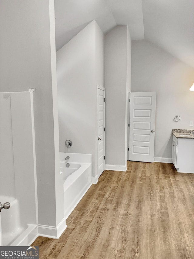 full bathroom with vanity, vaulted ceiling, a bath, and wood finished floors