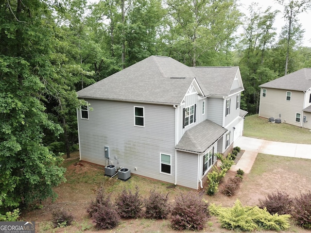 exterior space with an attached garage, driveway, central AC unit, and a shingled roof