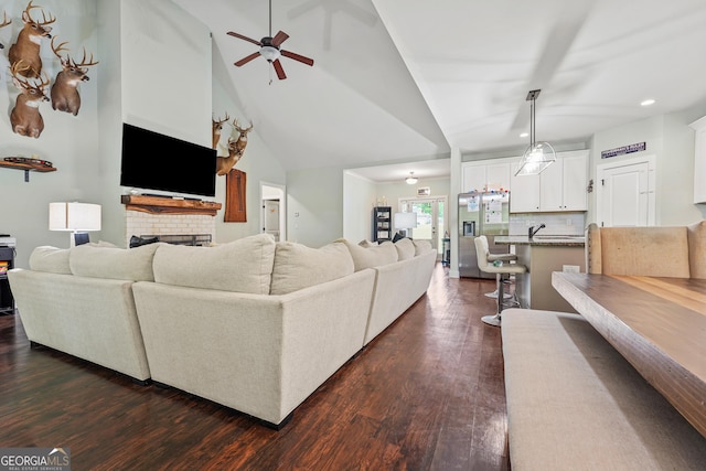 living room featuring a brick fireplace, lofted ceiling, ceiling fan, dark wood-style floors, and recessed lighting