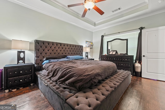 bedroom with crown molding, a raised ceiling, wood finished floors, and visible vents