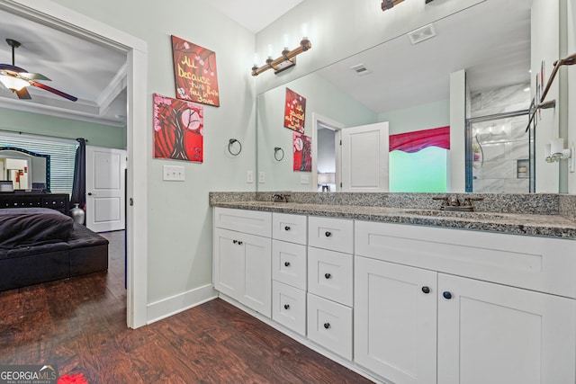full bathroom with double vanity, a stall shower, wood finished floors, a sink, and baseboards