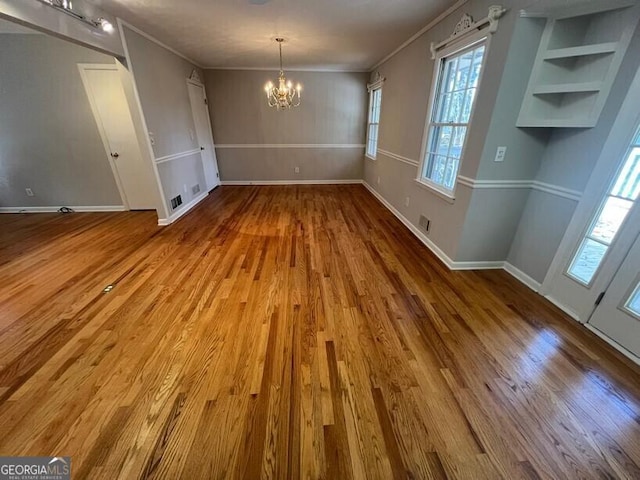 unfurnished dining area featuring baseboards, ornamental molding, wood finished floors, and a notable chandelier