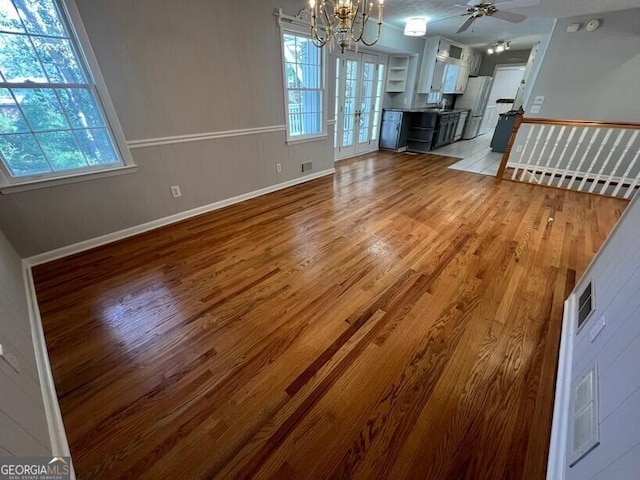 unfurnished living room with light wood finished floors, ceiling fan with notable chandelier, and a healthy amount of sunlight