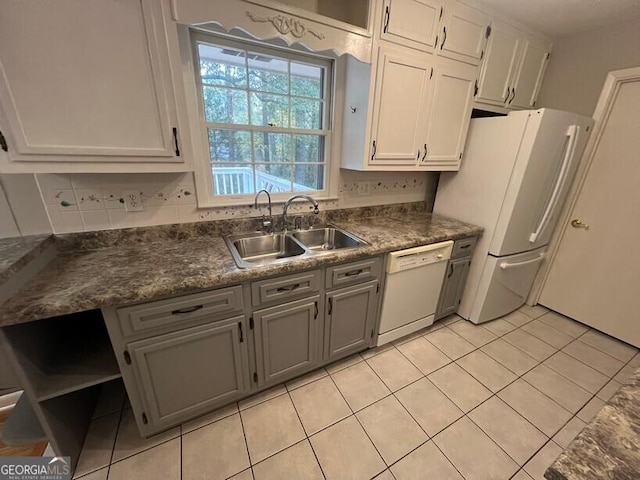 kitchen featuring dark countertops, white appliances, white cabinetry, a sink, and light tile patterned floors