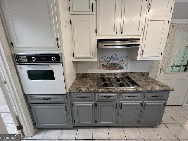 kitchen featuring stainless steel cooktop, light tile patterned floors, tasteful backsplash, gray cabinetry, and white oven