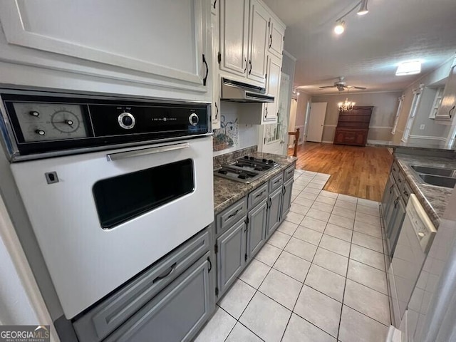 kitchen featuring white appliances, gray cabinets, open floor plan, light tile patterned floors, and under cabinet range hood