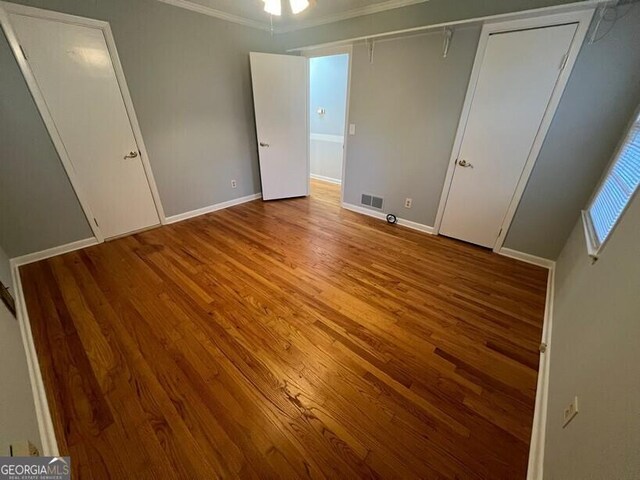 unfurnished bedroom with visible vents, ornamental molding, and wood finished floors