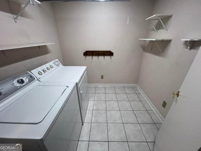 clothes washing area featuring laundry area, baseboards, light tile patterned flooring, and washing machine and clothes dryer
