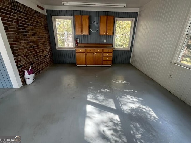 unfurnished living room with plenty of natural light, brick wall, and unfinished concrete floors