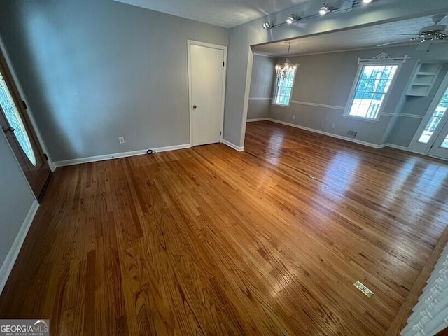 empty room featuring baseboards, ceiling fan with notable chandelier, and wood finished floors