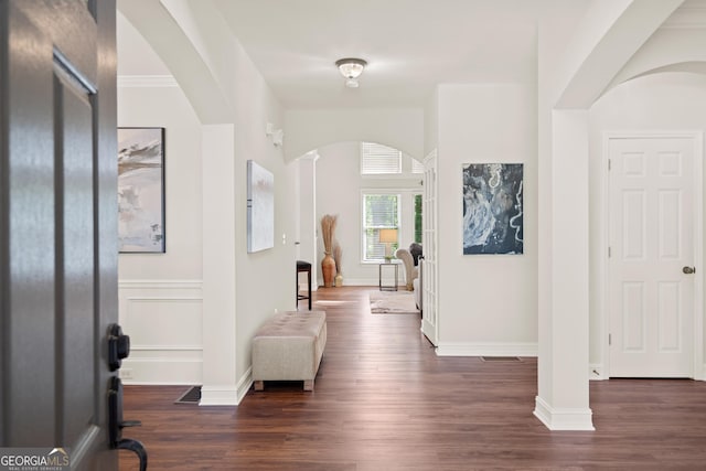 foyer with arched walkways, baseboards, and dark wood-type flooring