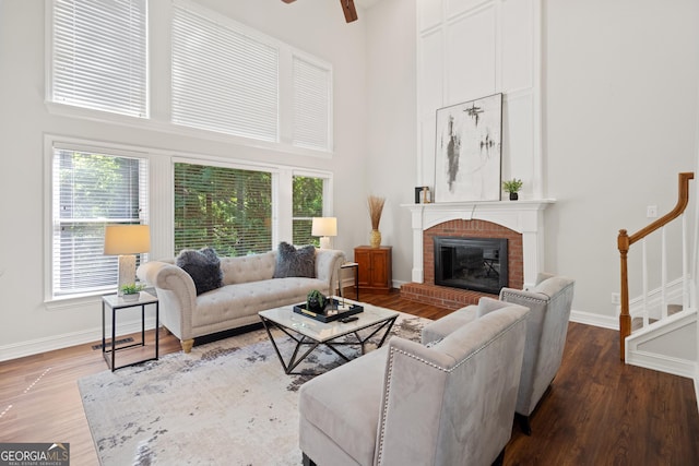 living area with baseboards, a high ceiling, a brick fireplace, and ceiling fan