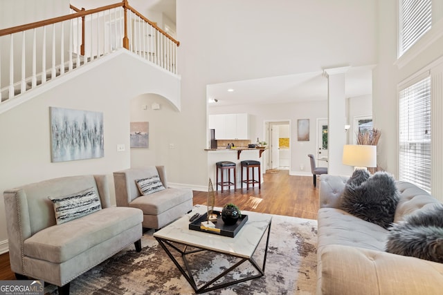 living area with arched walkways, baseboards, wood finished floors, a towering ceiling, and visible vents