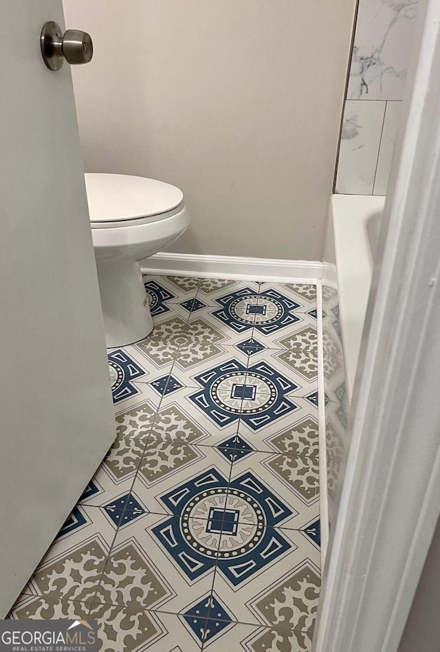 bathroom featuring tile patterned floors, toilet, baseboards, and a tub to relax in