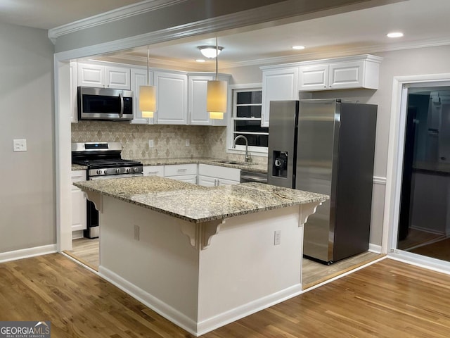 kitchen featuring stainless steel appliances, a sink, ornamental molding, light wood finished floors, and white cabinetry