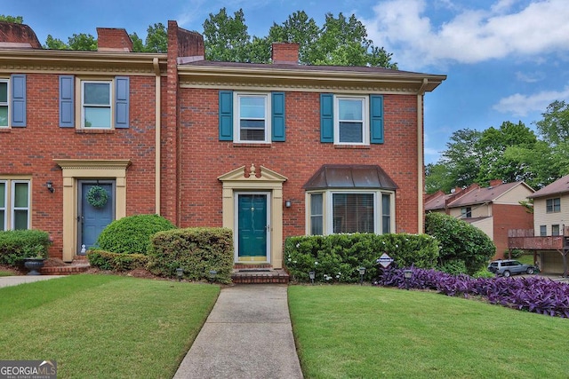 view of front facade with a chimney, a front yard, and brick siding