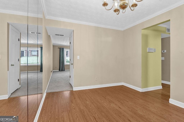 spare room featuring wood finished floors, a chandelier, baseboards, a textured ceiling, and crown molding