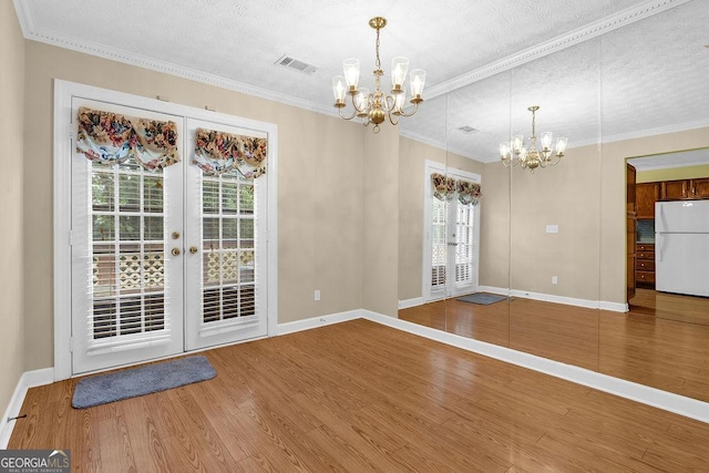 unfurnished dining area with french doors, a chandelier, baseboards, wood finished floors, and ornamental molding