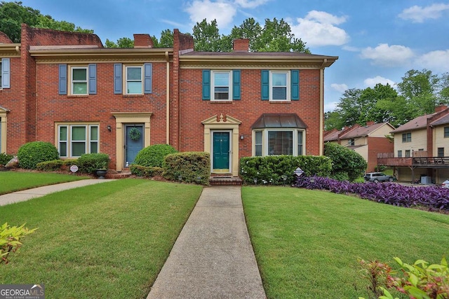 view of property with a chimney, a front lawn, and brick siding