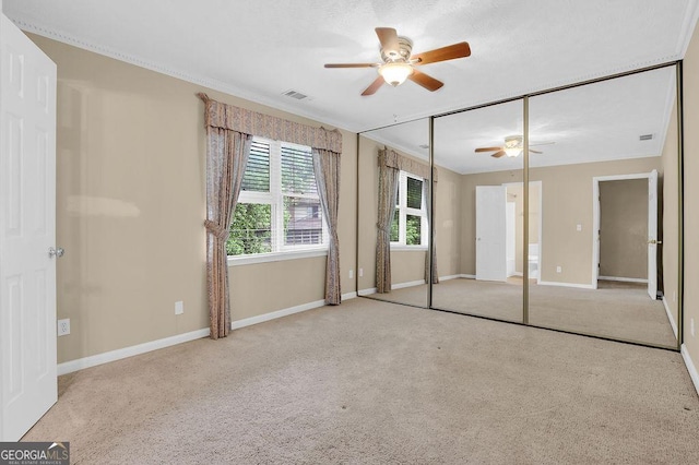unfurnished bedroom with carpet floors, baseboards, crown molding, a ceiling fan, and a closet