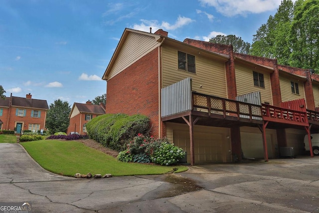 back of house featuring a garage, a chimney, concrete driveway, a lawn, and central AC