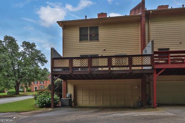 rear view of property with an attached garage, a chimney, and central air condition unit