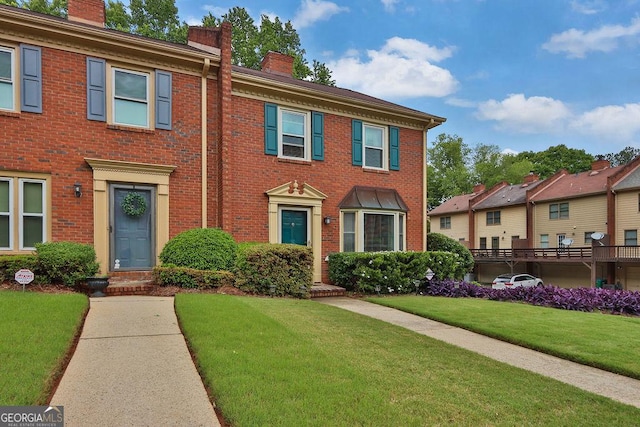 view of front of home featuring a chimney, brick siding, and a front yard